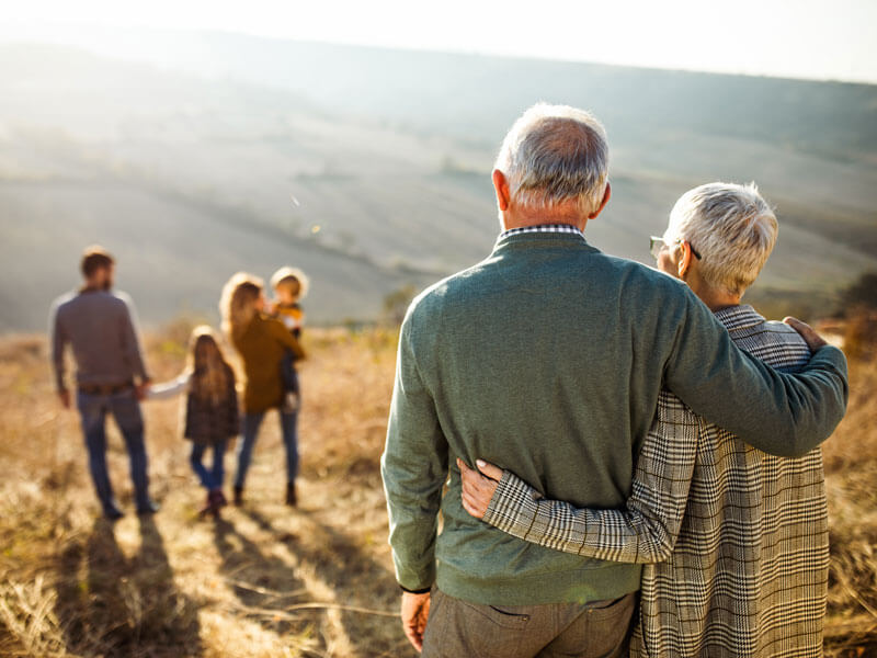 Back view of embraced grandparents looking at their family in the distance